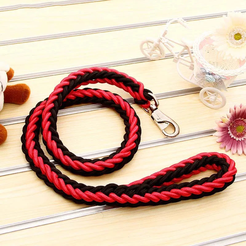 Red and black braided dog leash on a light wooden surface with decorative items.