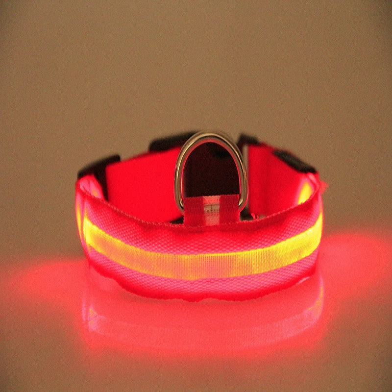 A red reflective dog collar with a bright yellow reflective stripe and a silver metal D-ring, shown glowing on a warm beige background with a red reflection below.
