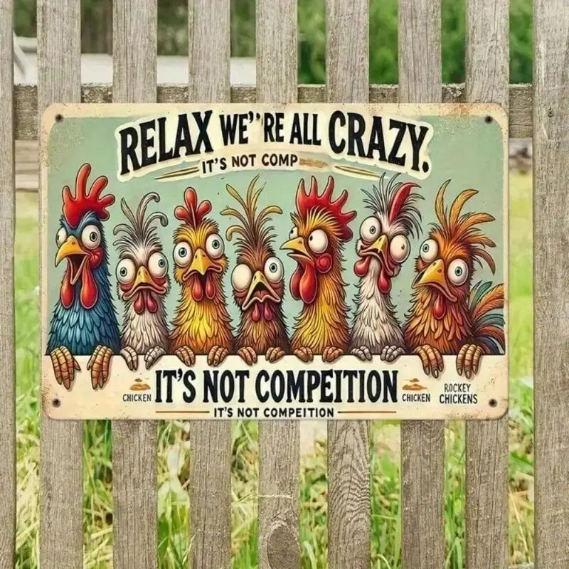 A rectangular metal sign with a vintage-style illustration of seven cartoon chickens and the text “RELAX WE’RE ALL CRAZY. IT’S NOT COMP” and “IT’S NOT COMPEITION,” mounted on a weathered wooden fence outdoors.