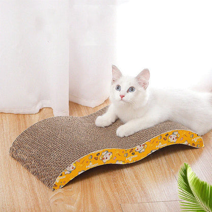White cat sitting on a floral-patterned cardboard scratcher on a wooden floor.