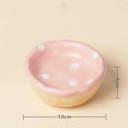 A small pink cupcake-shaped dish with white polka dots on the top and a pale yellow fluted base, shown on a beige background with dimension lines indicating 10 cm width and 4 cm height.