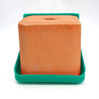 An orange rectangular foam block with a circular hole on top, resting inside a green plastic tray, photographed against a plain white background.