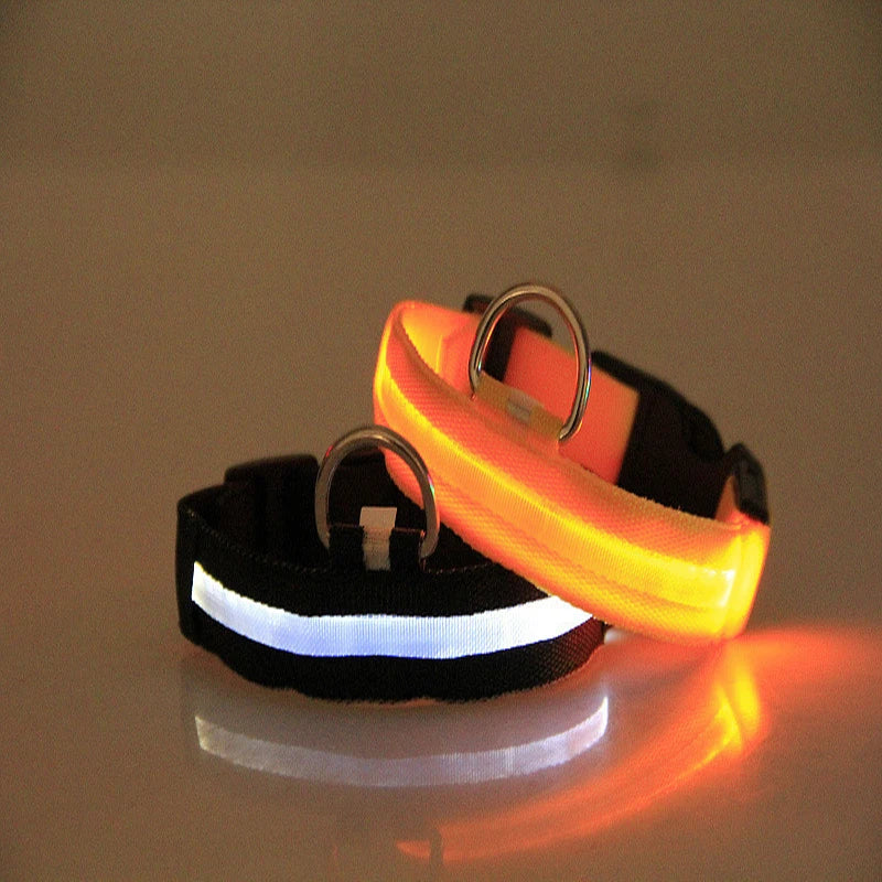 Two LED dog collars, one black and one orange, on a reflective surface with a brown background.
