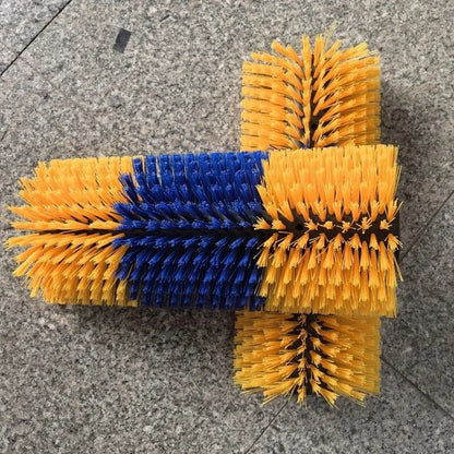 A dual-bristle cleaning brush with yellow and blue bristles arranged in a cross-like shape, photographed on a gray stone tile floor.
