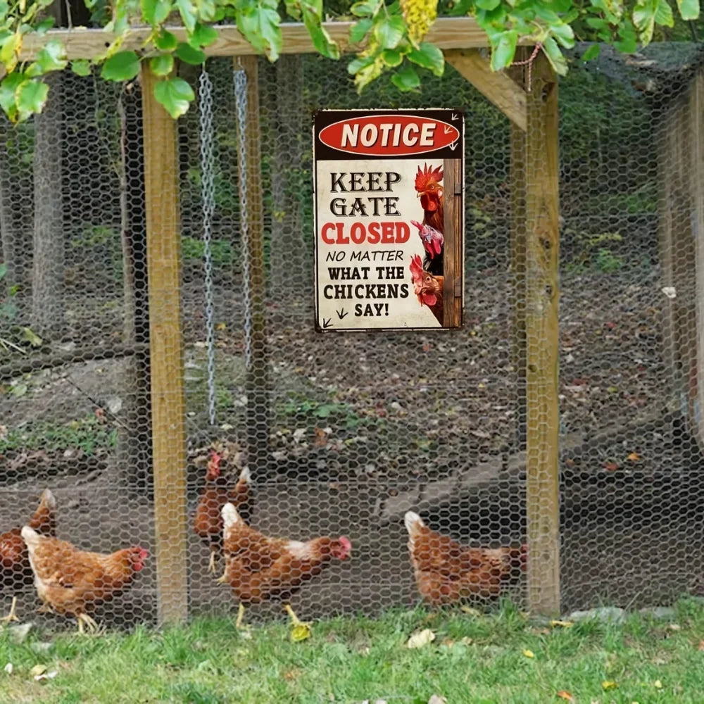 A rectangular metal sign with a red header reading 'NOTICE' and the phrase 'KEEP GATE CLOSED NO MATTER WHAT THE CHICKENS SAY!' hangs on a wooden chicken coop fence. Several brown chickens are visible behind the wire mesh in a backyard setting with trees and grass.