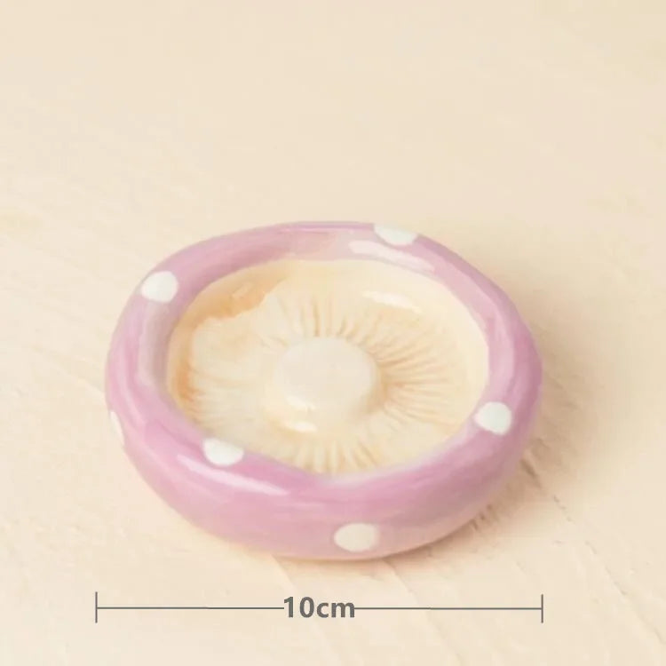 A small mushroom-shaped dish or tray in pastel pink and cream with white polka dots, shown on a light beige surface with a 10cm width measurement marker below.
