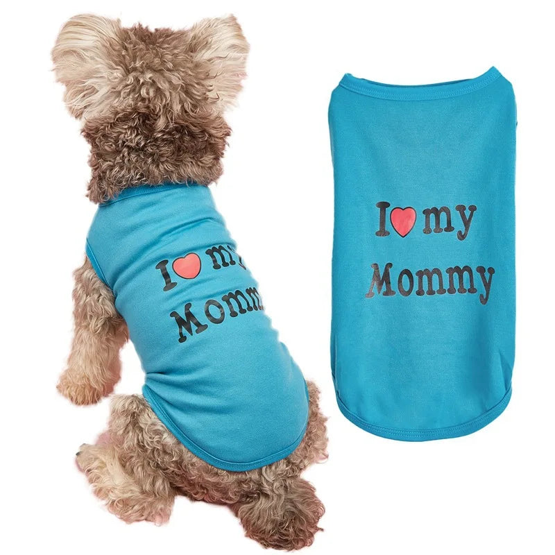 A small fluffy dog wearing a bright blue pet shirt with 'I [heart] my Mommy' printed on the back, shown next to a flat view of the same shirt on a white background.