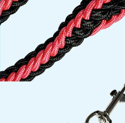 A close-up of a braided rope leash or lead in alternating black and pink strands, with a metal clasp partially visible in the lower right corner against a light blue background.