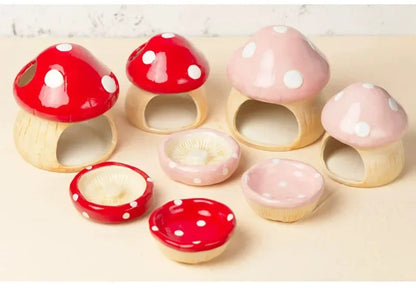A set of small mushroom-shaped ceramic or wooden containers in red and pink with white polka dots, arranged on a light beige surface against a pale background.