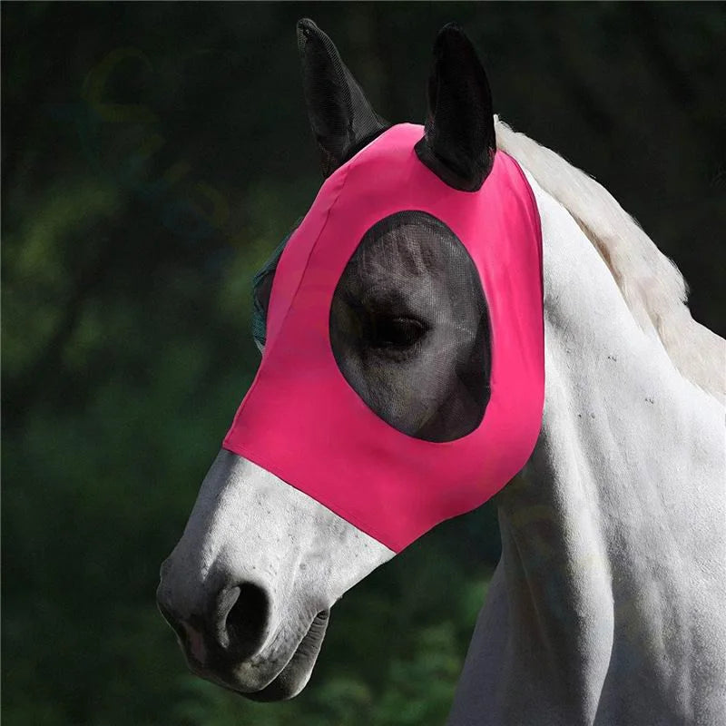 A close-up of a white horse wearing a bright pink horse fly mask, set against a dark, blurred outdoor background.